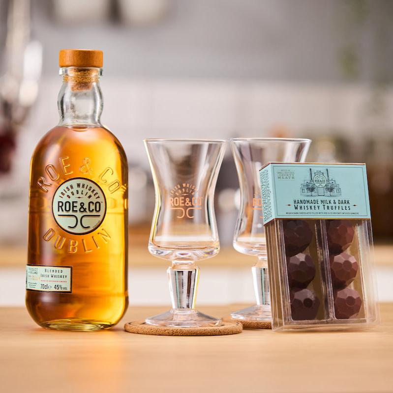 Image of Roe & Co Whiskey with two Irish coffee glasses on cork coasters and a pack of chocolate Whiskey truffles