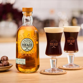 Image of Roe & Co Whiskey with two  glasses containing Irish coffees on cork coasters and a plate of chocolate Whiskey truffles